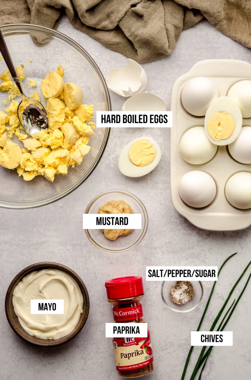 step-by-step flat lay showing halved hard boiled eggs, yolk filling in piping bag, sliced olives, and red hot sauce on a dark surface