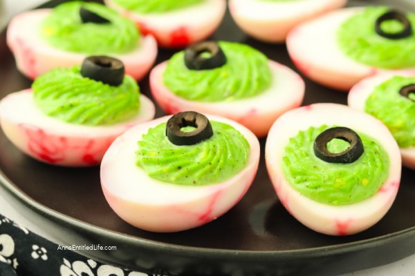 close-up of a single eyeball deviled egg on a dark slate board showing bloodshot hot sauce veins and olive pupil in sharp detail