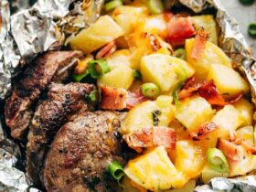 Foil packet steak and potato hash opened and steaming on a wooden board, showing golden potatoes, seared steak bites, and crispy bacon with fresh herb garnish