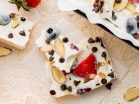 overhead shot of frozen greek yogurt berry bark broken into shards on a white marble surface surrounded by fresh berries and mint leaves