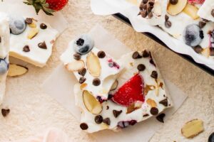 overhead shot of frozen greek yogurt berry bark broken into shards on a white marble surface surrounded by fresh berries and mint leaves