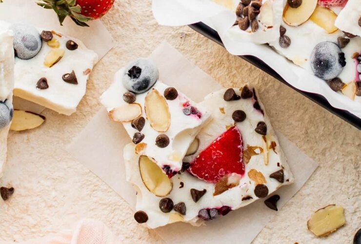 overhead shot of frozen greek yogurt berry bark broken into shards on a white marble surface surrounded by fresh berries and mint leaves
