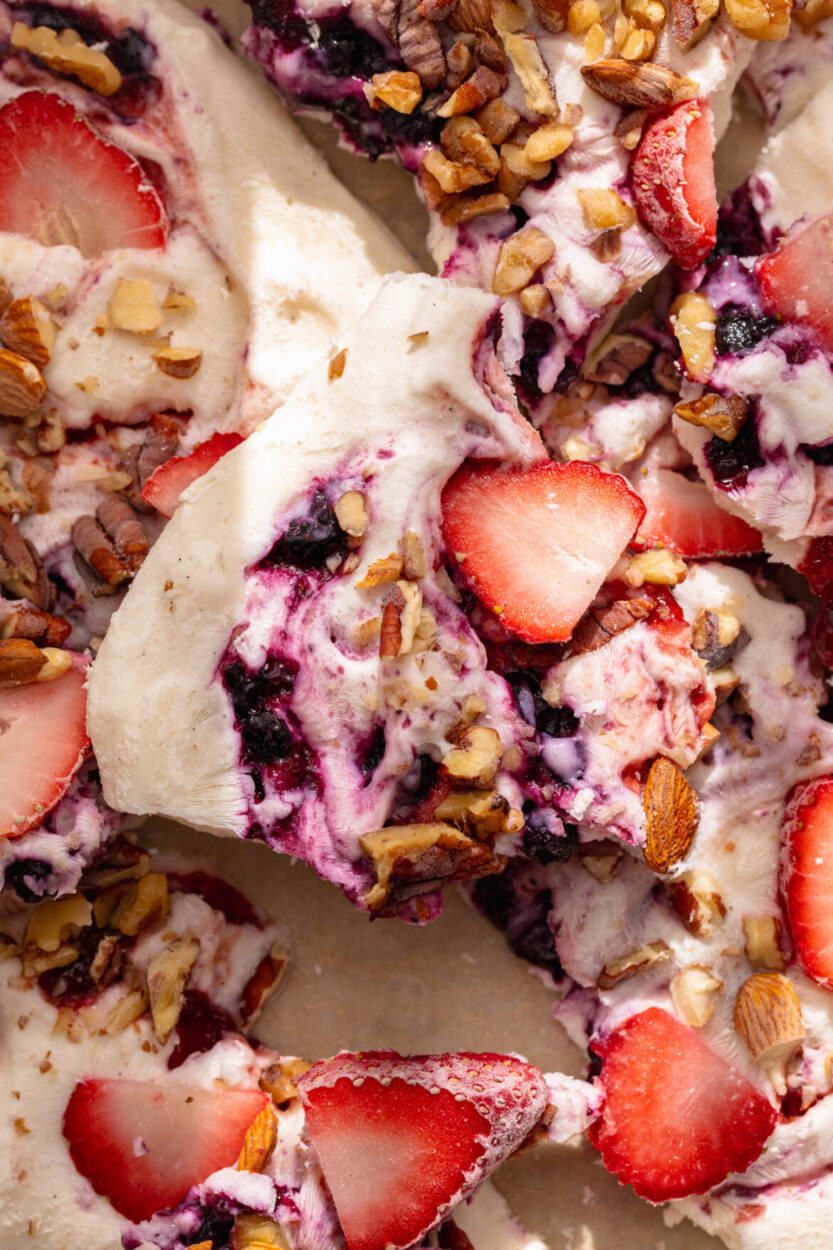 close-up of a hand holding a broken piece of frozen greek yogurt berry bark showing the creamy interior with blueberries and raspberries embedded throughout