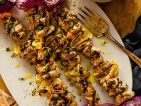 Greek Chicken Souvlaki skewers beautifully plated on a wooden board with pita bread, tzatziki, lemon wedges, and fresh herbs