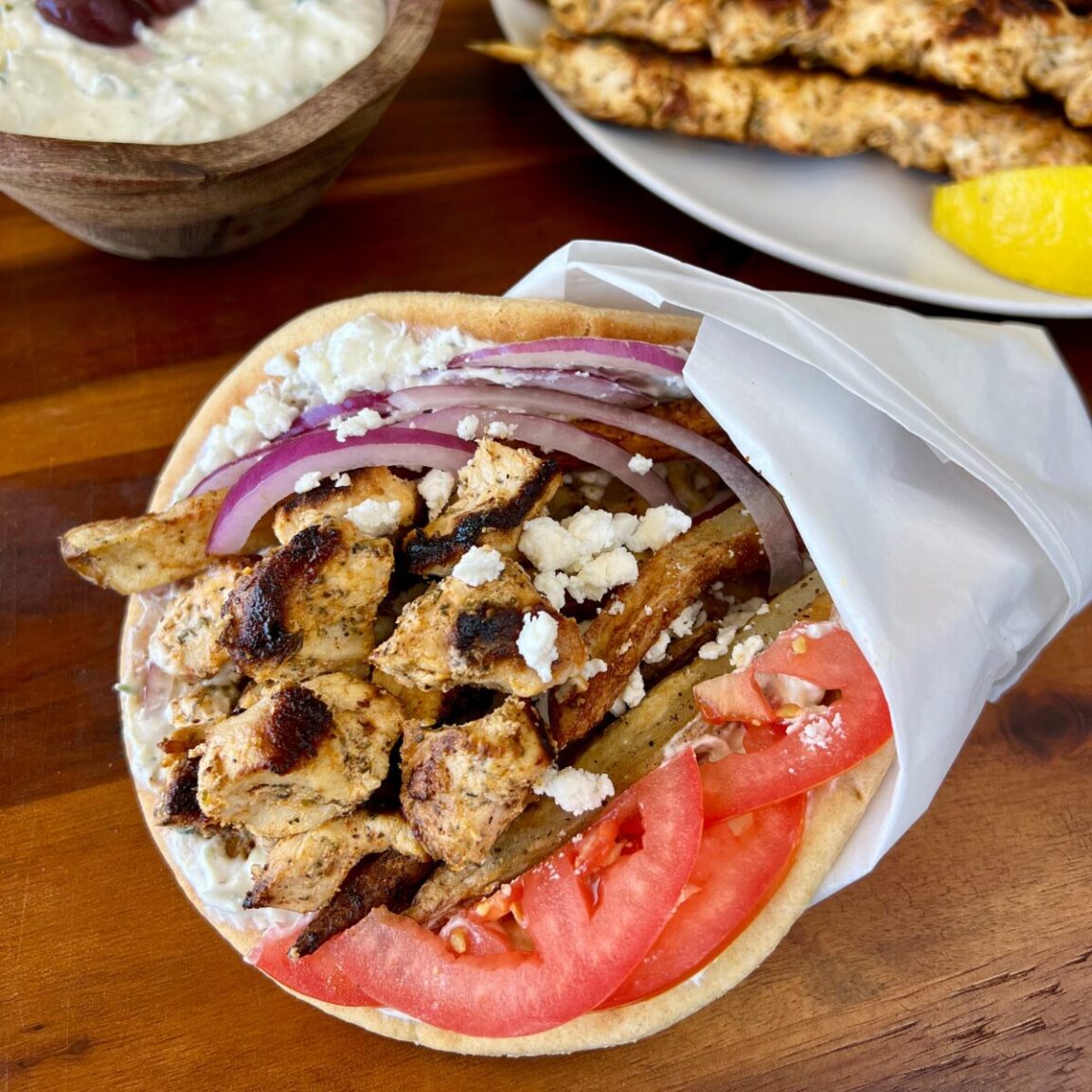 Close-up of Greek Chicken Souvlaki wrapped in warm pita with tzatziki sauce, fresh tomatoes, red onion, and herbs — ready to eat