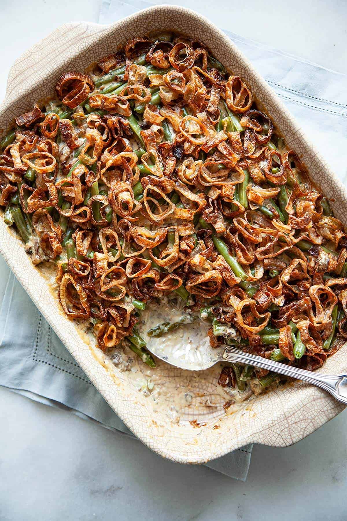 Close-up of a serving spoon lifting a portion of green bean casserole from scratch showing the creamy mushroom sauce coating the beans and crispy golden shallots on top