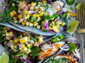Grilled fish tacos with corn salsa served on a rustic wooden board, garnished with fresh cilantro, lime wedges, and charred corn