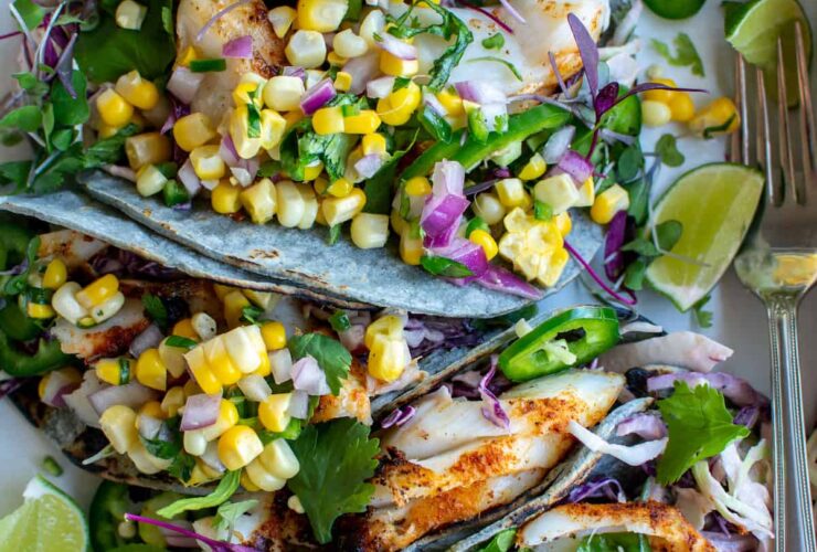 Grilled fish tacos with corn salsa served on a rustic wooden board, garnished with fresh cilantro, lime wedges, and charred corn