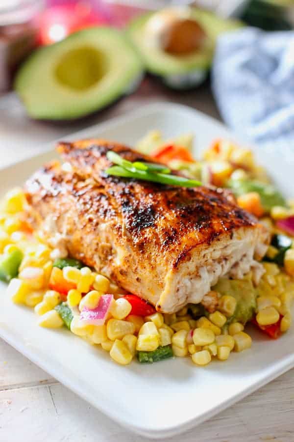 Spice-rubbed mahi-mahi fillets on a grill grate alongside ears of corn, with a small bowl of salsa ingredients nearby