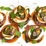 Grilled zucchini caprese stacks beautifully plated on a white marble board, drizzled with balsamic glaze and garnished with fresh basil leaves