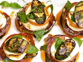 Grilled zucchini caprese stacks beautifully plated on a white marble board, drizzled with balsamic glaze and garnished with fresh basil leaves