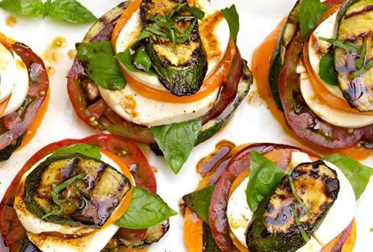 Grilled zucchini caprese stacks beautifully plated on a white marble board, drizzled with balsamic glaze and garnished with fresh basil leaves