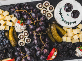 A beautifully styled Halloween charcuterie board with cheese ghosts, salami roses, black grapes, olives, and crackers arranged on a dark slate board with Halloween decorations