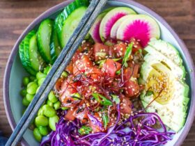 Hawaiian Poke Bowl beautifully plated in a white bowl with glossy soy-marinated ahi tuna, avocado slices, edamame, cucumber, pickled ginger, sriracha mayo drizzle, and sesame seeds on sushi rice