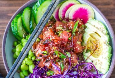 Hawaiian Poke Bowl beautifully plated in a white bowl with glossy soy-marinated ahi tuna, avocado slices, edamame, cucumber, pickled ginger, sriracha mayo drizzle, and sesame seeds on sushi rice