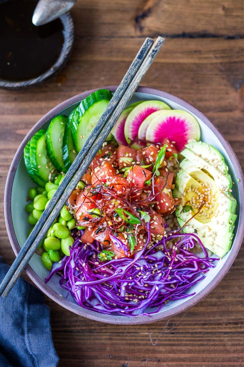 Hawaiian Poke Bowl beautifully plated in a white bowl with glossy soy-marinated ahi tuna, avocado slices, edamame, cucumber, pickled ginger, sriracha mayo drizzle, and sesame seeds on sushi rice