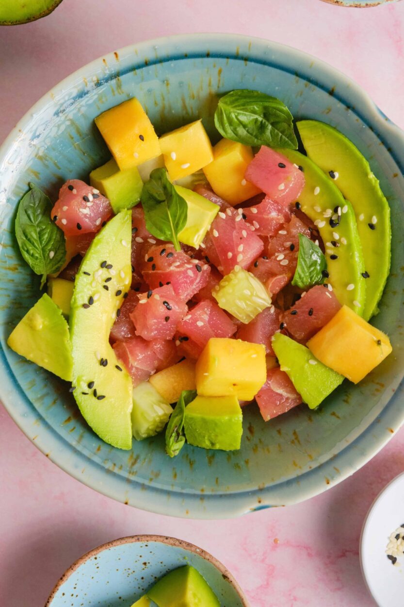 Close-up of Hawaiian Poke Bowl showing glossy soy-marinated ahi tuna cubes glistening with sesame seeds, creamy avocado slices, bright orange tobiko, and a drizzle of sriracha mayo over sushi rice