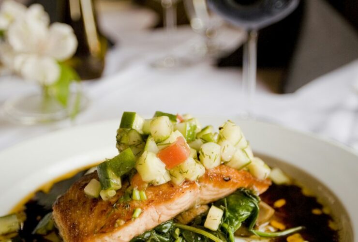 Herb-crusted salmon fillet with golden herb crust resting on a bed of roasted summer vegetables including zucchini, cherry tomatoes, and bell peppers, plated on a white dish with lemon wedges and fresh parsley