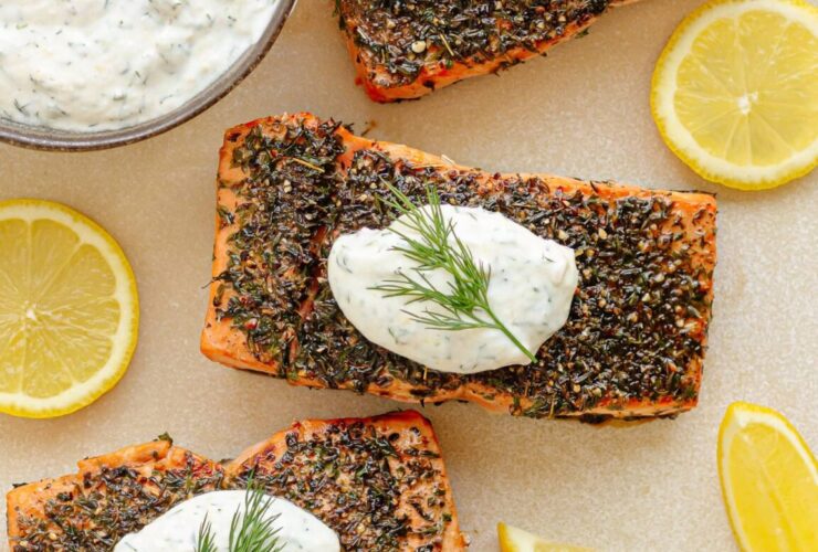 herb crusted salmon with summer vegetables beautifully plated on a white serving dish, garnished with fresh dill and lemon wedges, roasted cherry tomatoes and zucchini surrounding the fillet