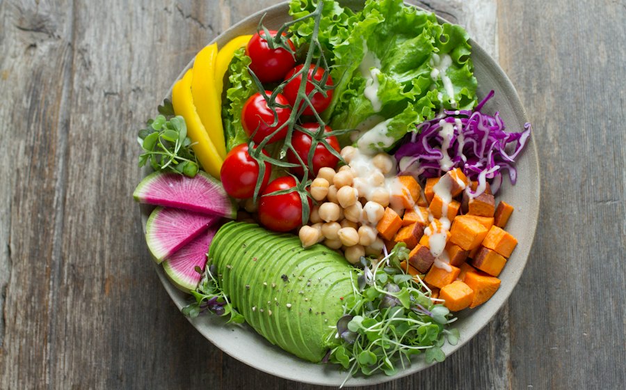 Overhead flat-lay of herb crusted salmon ingredients including fresh salmon fillets, bunches of parsley, dill, basil, lemon, garlic cloves, cherry tomatoes, zucchini, and bell peppers on a marble surface