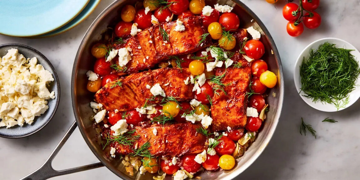 flat lay ingredients shot showing fresh salmon fillets, bowls of chopped parsley and dill, cherry tomatoes, sliced zucchini, bell peppers, lemon, garlic, and Dijon mustard on a marble surface
