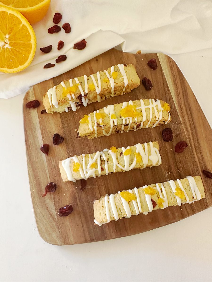 Fresh cranberries, sugar, orange halves, and zest arranged on a wooden cutting board with a small saucepan