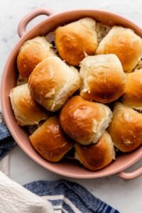 Honey butter dinner rolls in a baking pan, golden brown and glistening with honey butter glaze, shot overhead on a rustic wooden table