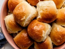 Honey butter dinner rolls in a baking pan, golden brown and glistening with honey butter glaze, shot overhead on a rustic wooden table