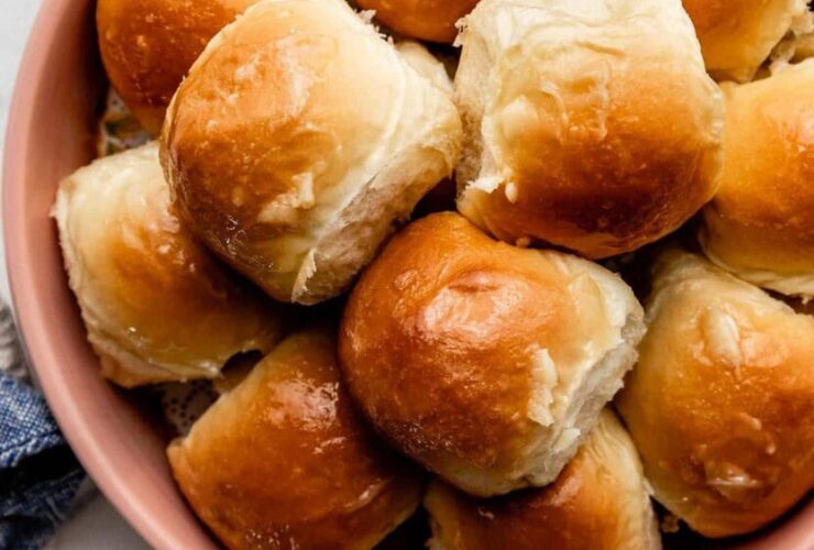 Honey butter dinner rolls in a baking pan, golden brown and glistening with honey butter glaze, shot overhead on a rustic wooden table