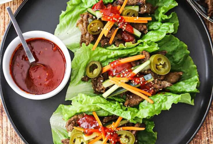 Korean BBQ lettuce wrap bowls beautifully plated on a rustic wooden board with vibrant garnishes, sesame seeds, and dipping sauce
