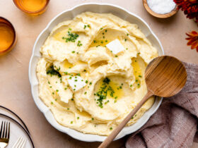 Make ahead mashed potatoes served in a large white bowl, topped with melted butter, fresh chives, and cracked black pepper on a holiday table setting