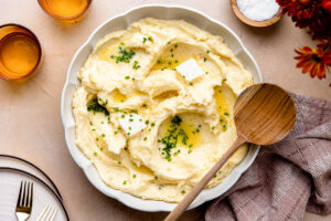 Make ahead mashed potatoes served in a large white bowl, topped with melted butter, fresh chives, and cracked black pepper on a holiday table setting