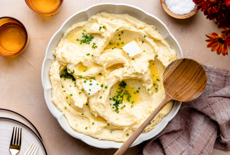 Make ahead mashed potatoes served in a large white bowl, topped with melted butter, fresh chives, and cracked black pepper on a holiday table setting