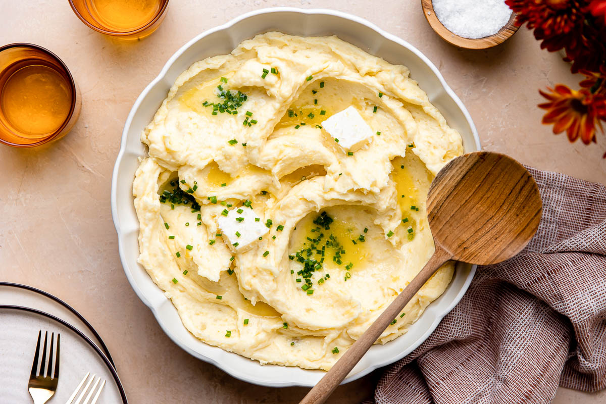 Make ahead mashed potatoes served in a large white bowl, topped with melted butter, fresh chives, and cracked black pepper on a holiday table setting