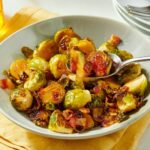 Maple roasted brussels sprouts with bacon on a white serving platter, caramelized and glossy with visible crispy bacon pieces