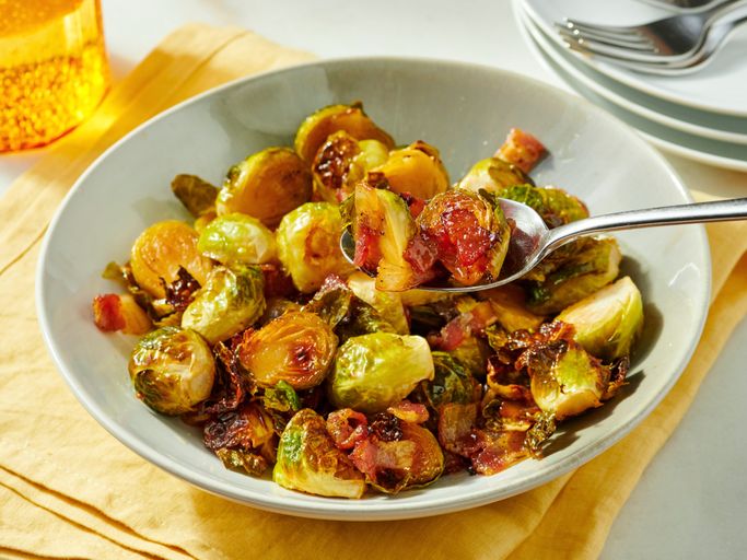 Maple roasted brussels sprouts with bacon on a white serving platter, caramelized and glossy with visible crispy bacon pieces