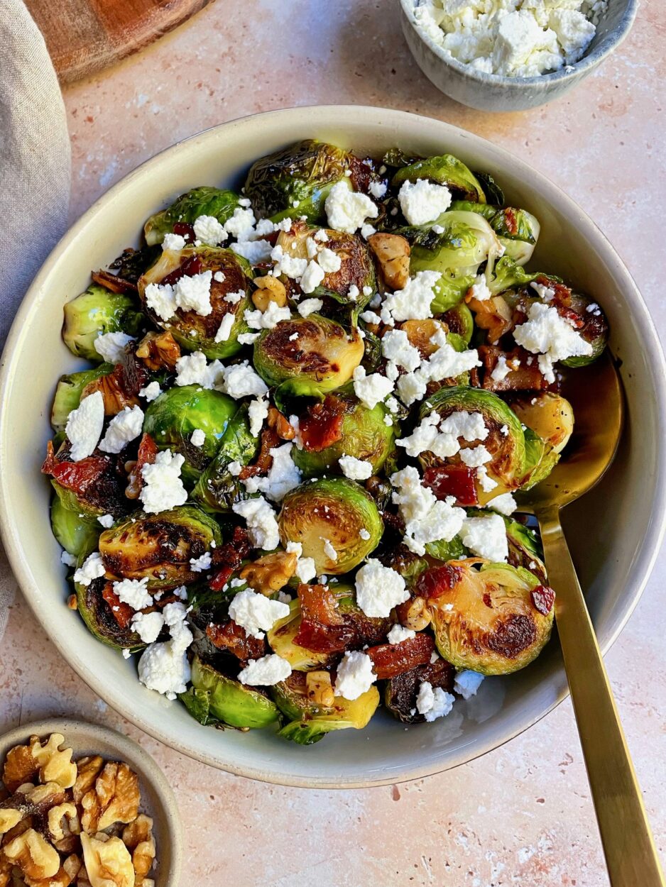 Brussels sprouts halved on a cutting board alongside strips of thick-cut bacon, maple syrup, garlic, and apple cider vinegar — ingredients for the recipe