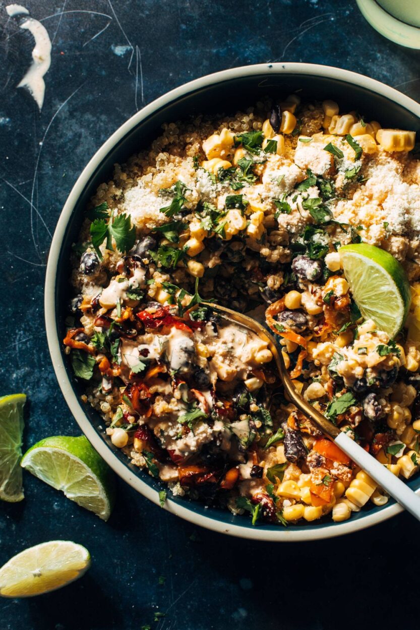 Overhead flat lay of Mexican street corn quinoa salad ingredients including charred corn kernels, dry quinoa, cotija cheese, lime, cilantro, chili powder, and mayonnaise on a marble surface