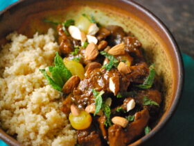Moroccan lamb tagine served in a traditional clay tagine pot with couscous, garnished with fresh cilantro, slivered almonds, and golden raisins on a rustic wooden table