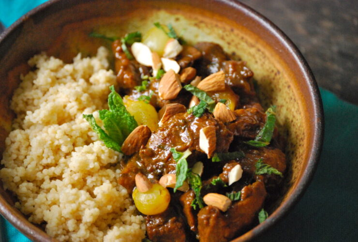 Moroccan lamb tagine served in a traditional clay tagine pot with couscous, garnished with fresh cilantro, slivered almonds, and golden raisins on a rustic wooden table