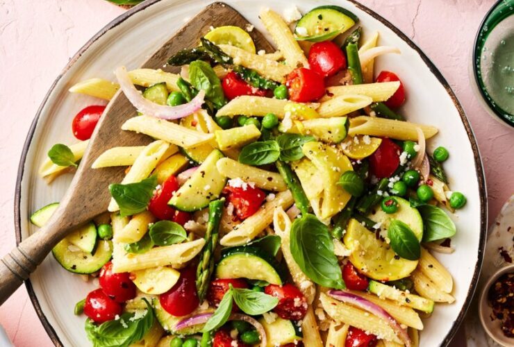 Pasta Primavera served in a wide white bowl with colorful summer vegetables, cherry tomatoes, zucchini, asparagus, and fresh basil, drizzled with olive oil and topped with shaved Parmesan
