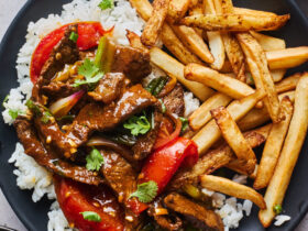 Peruvian Lomo Saltado served in a large bowl with golden French fries, seared beef strips, tomatoes, and red onions garnished with fresh cilantro
