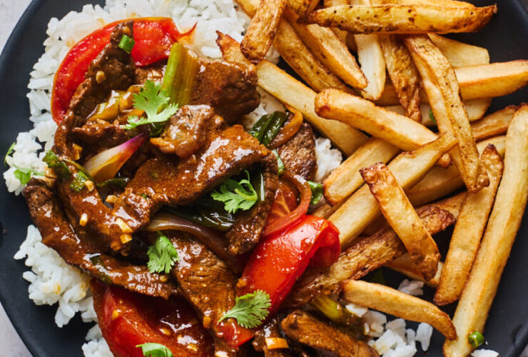 Peruvian Lomo Saltado served in a large bowl with golden French fries, seared beef strips, tomatoes, and red onions garnished with fresh cilantro