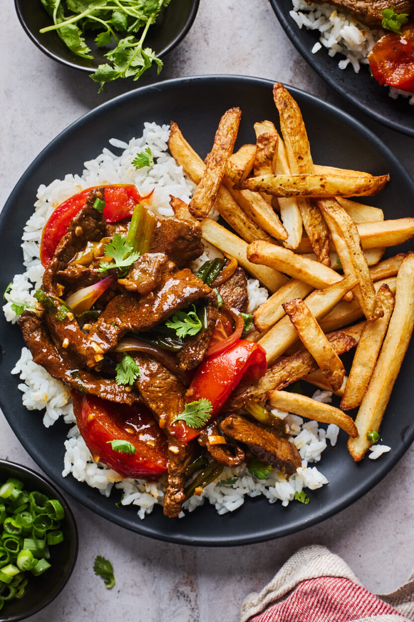 Peruvian Lomo Saltado served in a large bowl with golden French fries, seared beef strips, tomatoes, and red onions garnished with fresh cilantro