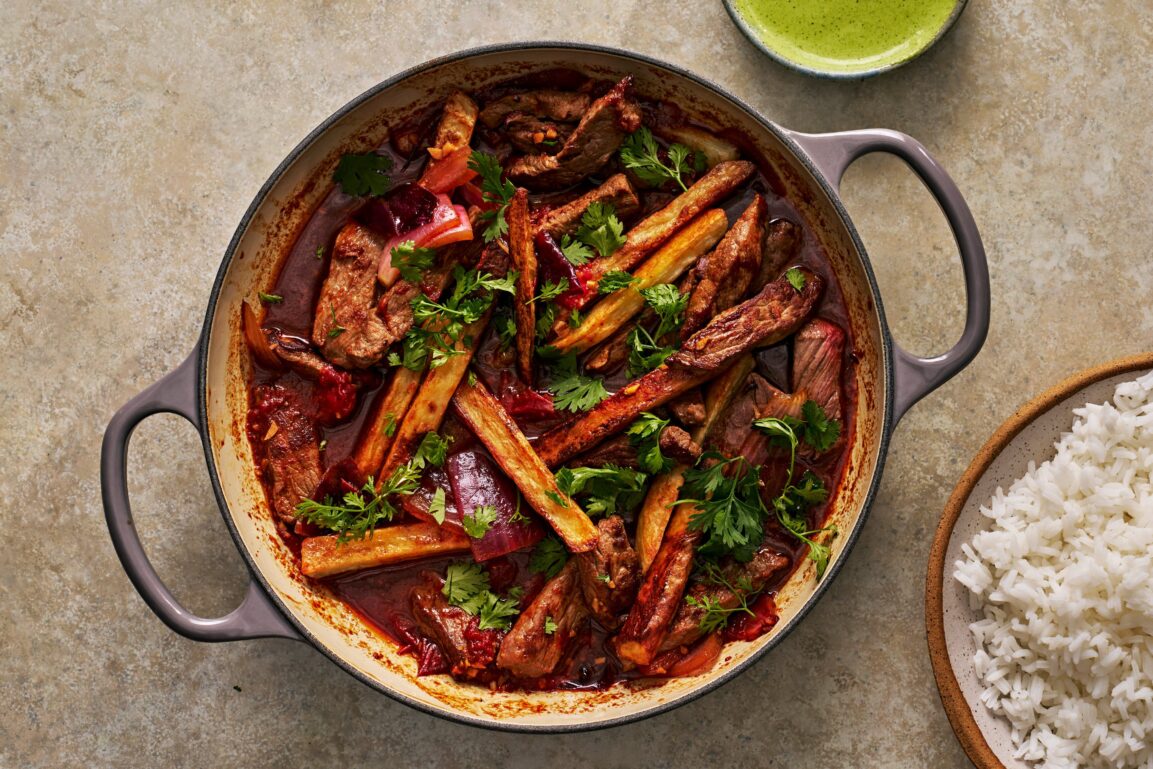 Sliced beef sirloin, ají amarillo paste, soy sauce, red onion, tomatoes, and fresh cilantro arranged on a wooden cutting board as prep ingredients for Lomo Saltado