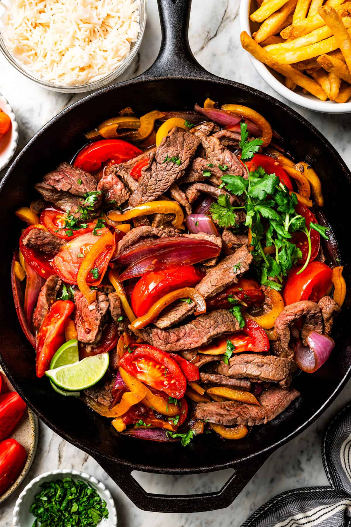 Close-up of Peruvian Lomo Saltado in a white bowl showing glossy soy-citrus glazed beef strips, golden fries, softened tomatoes and onions topped with fresh cilantro leaves