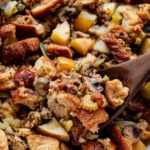 Sausage and herb stuffing in a golden baking dish, crispy bread cubes on top, fresh thyme garnish, rustic Thanksgiving table setting
