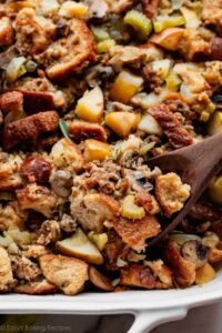 Sausage and herb stuffing in a golden baking dish, crispy bread cubes on top, fresh thyme garnish, rustic Thanksgiving table setting