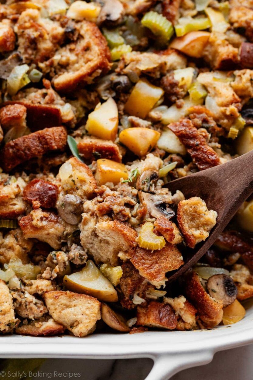 Sausage and herb stuffing in a golden baking dish, crispy bread cubes on top, fresh thyme garnish, rustic Thanksgiving table setting