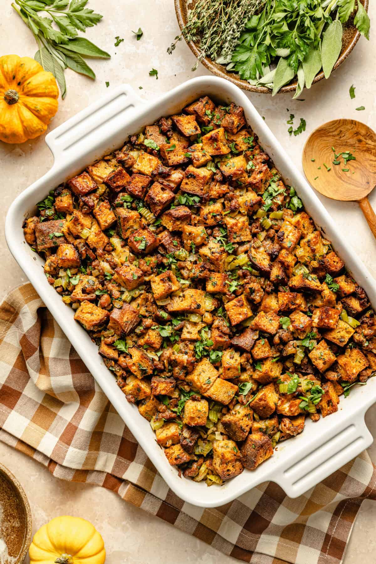 Ingredients for sausage stuffing laid out flat — cubed bread, Italian sausage, fresh thyme, sage, celery, onions, eggs, and chicken broth
